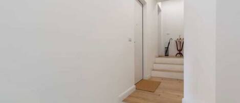 A narrow, white-walled hallway with wooden steps leading to a door at the end.
