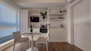Ein zeitgemäßer Essbereich mit einem weißen Tisch und Stühlen, einem Fernseher an der Wand und Meerblick durch ein Fenster.