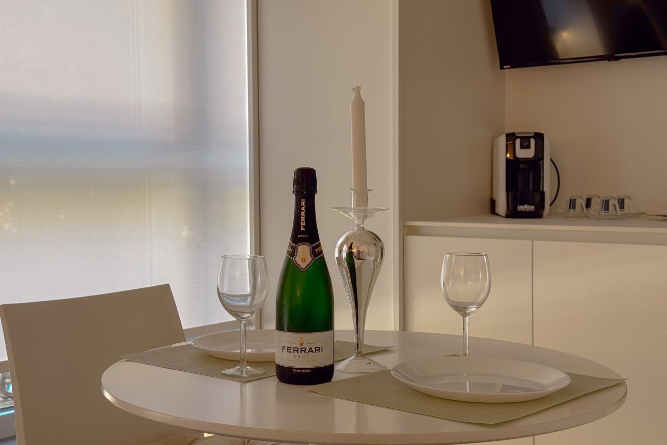 Une table avec une bouteille de vin Ferrari Brut, deux verres à vin, une bougie et une machine à café.