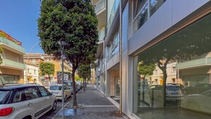 Straßenansicht mit parkenden Autos, Bürgersteig und Gebäuden mit großen Fenstern.