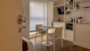 Ein modernes Interieur mit einer weißen Tür, einem Essbereich mit Tisch und Stühlen sowie einem weißen Regal.