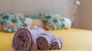 A neatly rolled purple towel on a yellow bedspread, with patterned pillows in the background. - San Gregorio House (Milano)