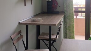 Une petite pièce comprenant un bureau, deux chaises, un téléviseur fixé au mur et une fenêtre avec des rideaux.