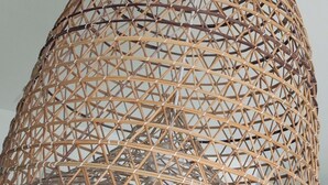 Un luminaire suspendu en forme de dôme, fabriqué à partir de fibres tressées, et doté d’une ampoule blanche.
