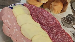 Une assiette garnie de tranches de salami, de fromage et de petits pains.