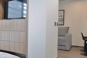 Ein modernes Zimmer mit integriertem Fernseher, grauem Sofa und schwarzem Sessel.