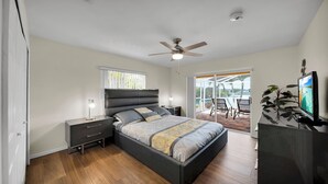 Un dormitorio moderno con cama, mesitas de noche, ventilador de techo y vistas al exterior.