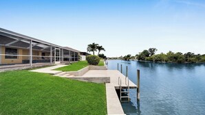 Un edificio moderno con un patio cubierto, césped y un canal con muelle.