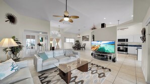 Un salón amplio con un sofá blanco, una mesa de centro de vidrio y un televisor de pantalla plana mostrando una vista panorámica.
