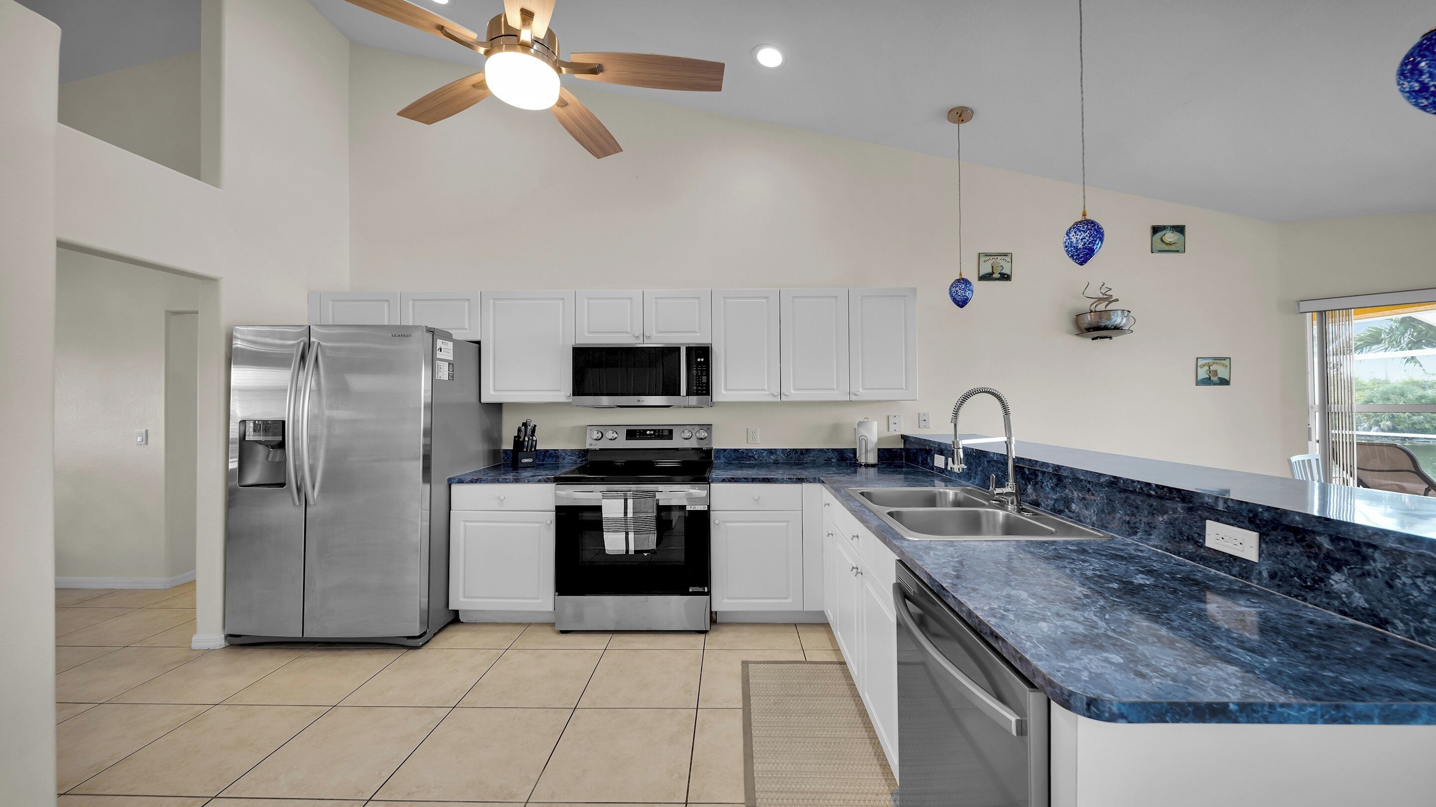Una cocina moderna con armarios blancos, electrodomésticos de acero inoxidable, una encimera de mármol azul y un ventilador de techo.