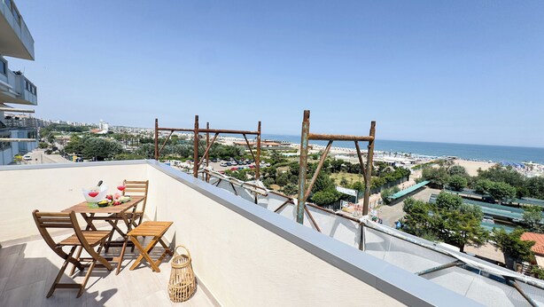 A balcony with a table set for two, overlooking a beach and cityscape. - Rooftop Blu Infinito by Ca-Sa Check (Chioggia)