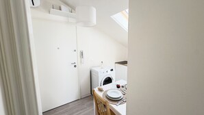 A laundry room with a washing machine, a small table with a plate and utensils, and a hanging lamp. - Rooftop Blu Infinito by Ca-Sa Check (Chioggia)