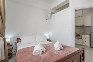 A bedroom with a bed, bedside tables, a fan, and a kitchenette. - Apartment 'Kallithea Beach' with Sea View, Wi-Fi and Air Conditioning (Myrtos)