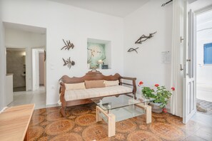 Un salon avec un canapé, une table basse en verre, une plante en pot et des œuvres d’art murales.