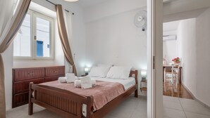 A bedroom with a wooden bed, white bedding, a bedside table with a lamp, and a window with curtains.