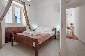 A bedroom with a wooden bed, white bedding, a bedside table with a lamp, and a window with curtains.