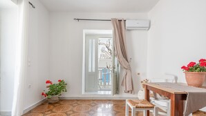 A room with a tiled floor, a white chair, a wooden table with a cloth, a potted plant, and a door leading to an outdoor area.