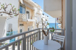 A balcony with a white table and chair, overlooking a coastal area with buildings and the sea.