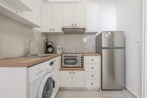 A compact kitchen with a washing machine, a coffee maker, an oven, and a stainless steel refrigerator. - Apartment 'Kallithea Beach' with Sea View, Wi-Fi and Air Conditioning (Myrtos)
