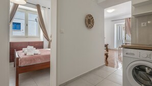 A bedroom with a bed, a washing machine, and a window with curtains.