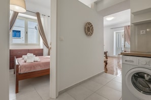 A bedroom with a bed, a washing machine, and a window with curtains.