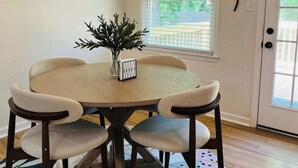 Comedor con mesa redonda, seis sillas, lámpara colgante, planta en maceta y ventana con persianas.