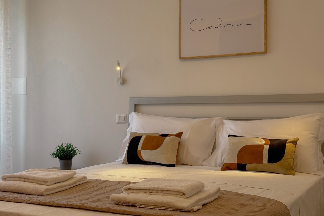 Un letto rifatto con cuscini, una pianta sul comodino e un quadro appeso alla parete.