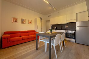 A modern kitchen with white cabinets, a dining table with chairs, and a red sofa.