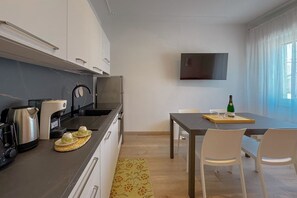 A modern kitchen with a flat-screen TV, a dining table with chairs, and a window with curtains.