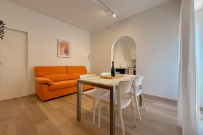 Ett modernt vardagsrum med en matplats, en soffa och ett kök i bakgrunden.