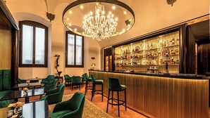 A bar area with a bar counter, green upholstered chairs, a chandelier, and a wine rack.
