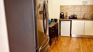 A compact kitchen with a stainless steel refrigerator, a tiled backsplash, a wooden floor, and a small dining area. - 7 Night Discount- Lagos Marina- Doublebed (Lagos)