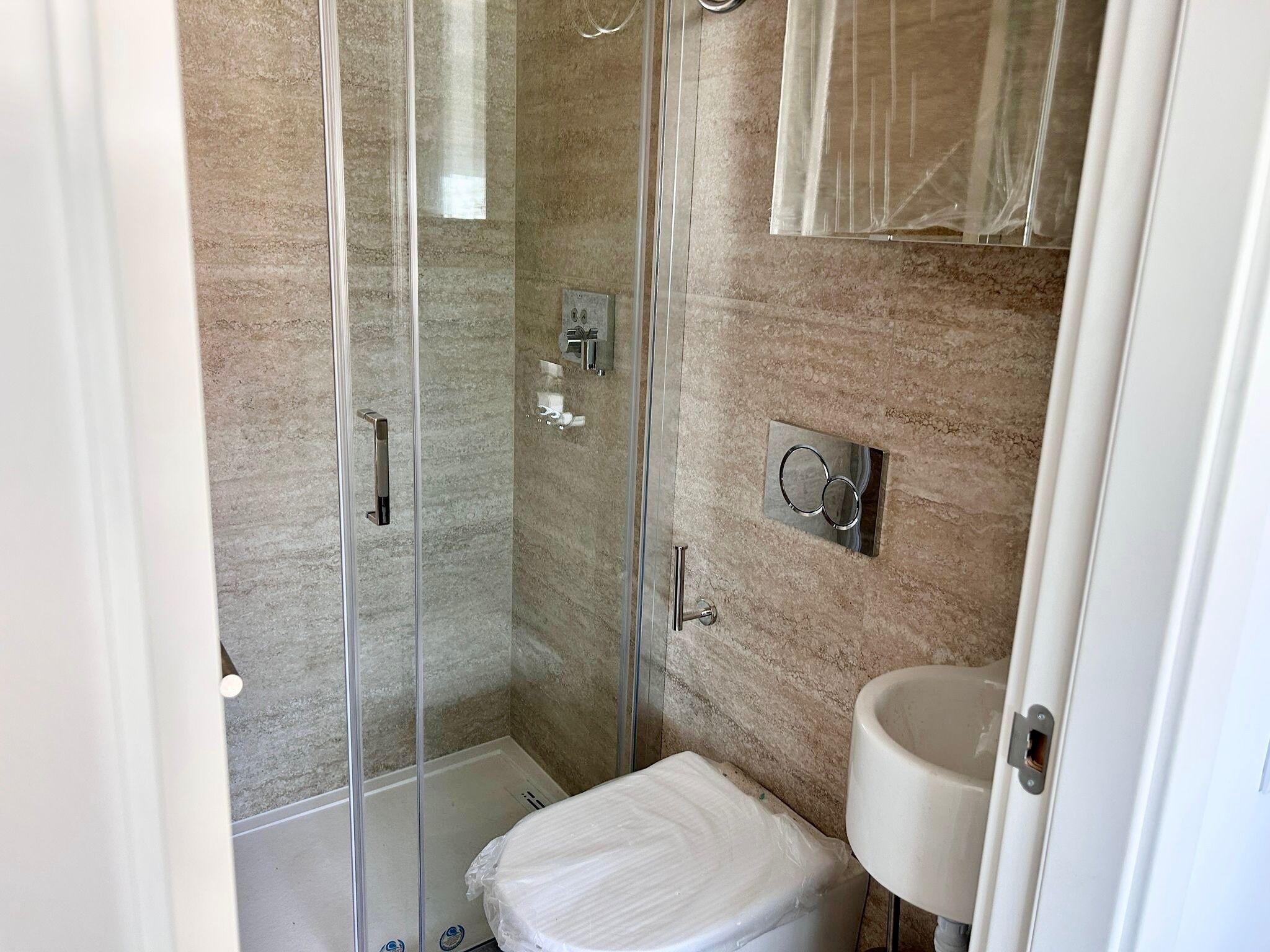 Un bany amb dutxa trencada per vidre, un vàter i un lavabo.