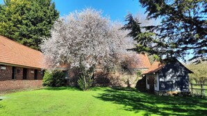 A brick building with a red-tiled roof, a small garden, and a tree with white blossoms. - Le Clos Saint Martin, charming gîte - 14 pers- Chic countryside 35mn from the sea (Cavron Saint Martin)