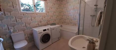 A bathroom with a washing machine, toilet, bathtub, and sink.