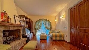 A living room with a fireplace, a sofa, an ottoman, and a television. - Cozy Home with Garden and Privacy (Spello)
