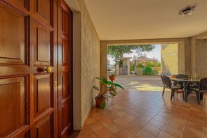 Eine Holztür, ein Blumentopf, eine geflieste Terrasse und ein Tisch mit Stühlen.