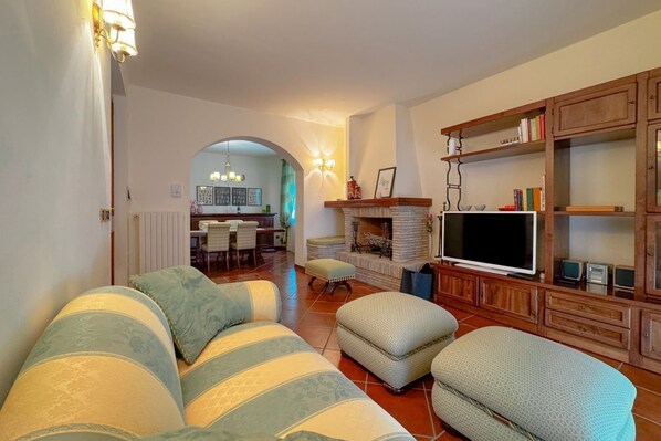 Ein Wohnzimmer mit einer Couch, Hocker, Fernseher, Kamin und Holzböden.