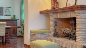 A cozy living room with a fireplace, a wooden bench, and a green ottoman. - Cozy Home with Garden and Privacy (Spello)