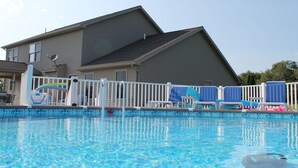 En swimmingpool med et hvidt hegn, blå liggestole og et hus i baggrunden.