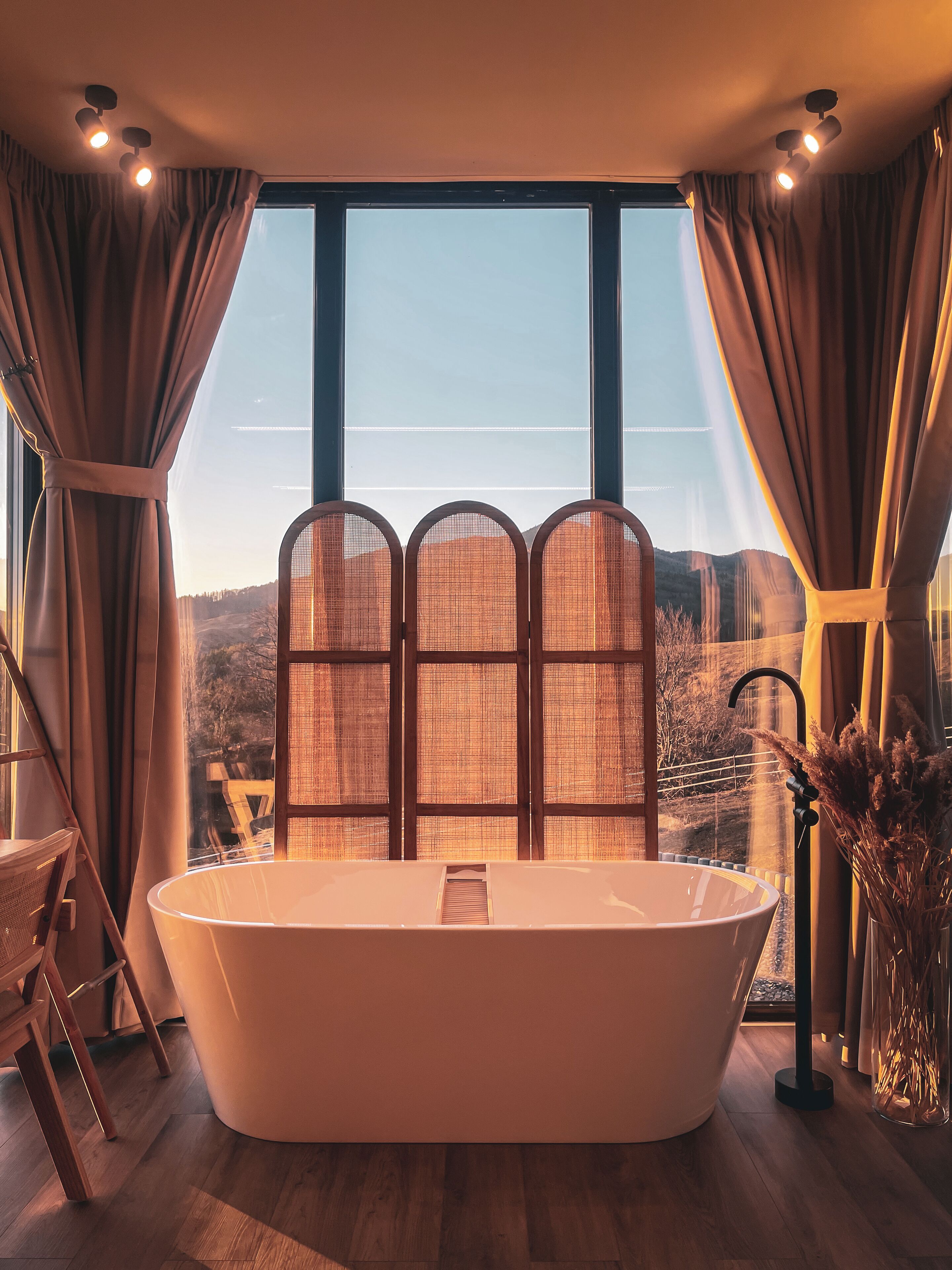 A modern bathroom with a freestanding bathtub, large windows, and a view of a mountainous landscape.