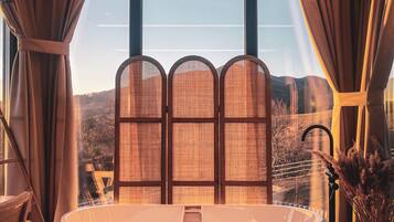 A modern bathroom with a freestanding bathtub, large windows, and a view of a mountainous landscape.