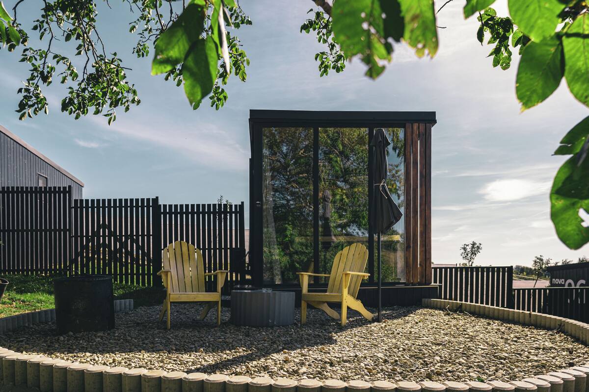 Een terras met twee Adirondack-stoelen, een vuurkuil en een glazen constructie.