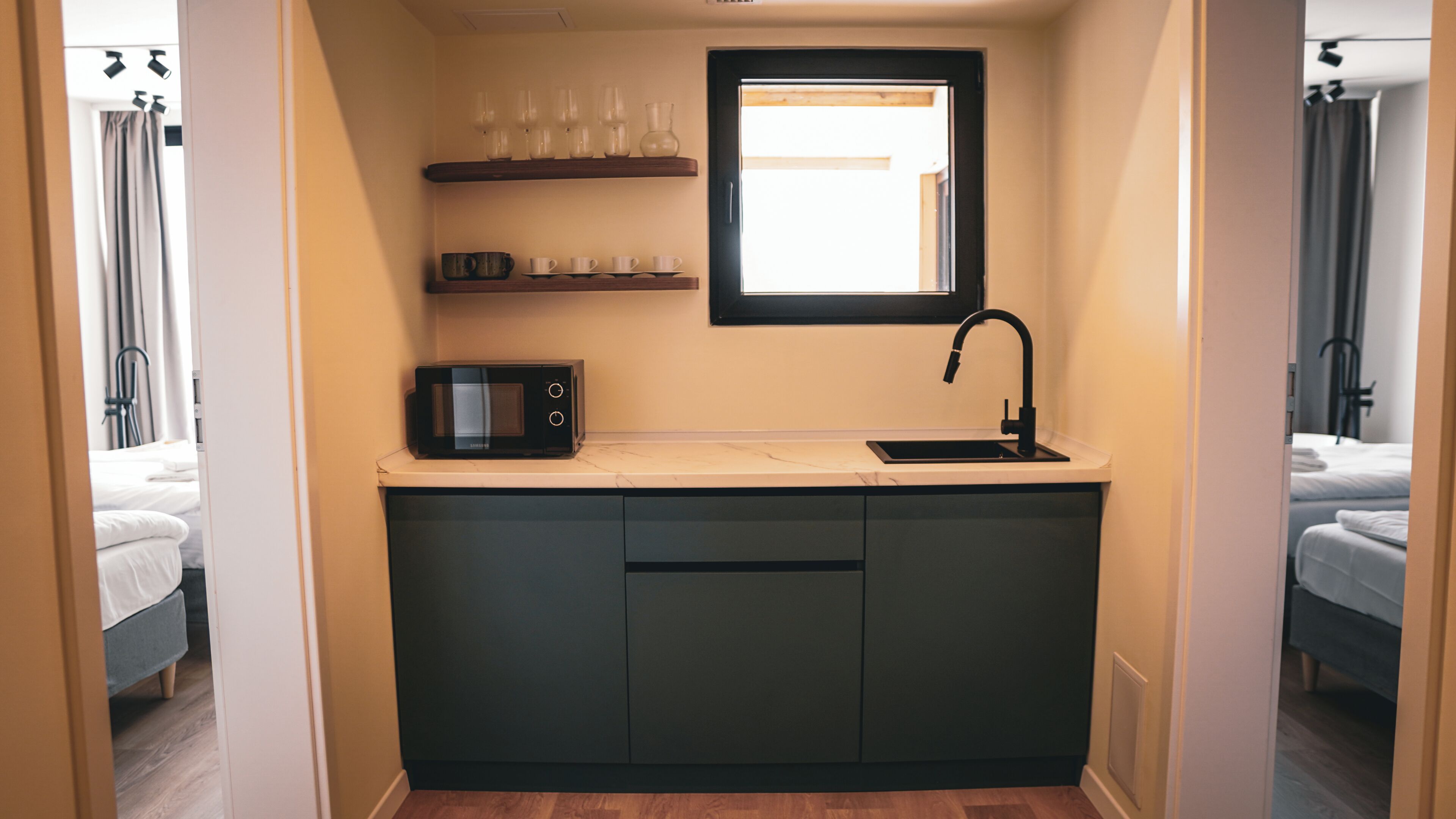 A compact kitchenette with a microwave, sink, and shelves above for glasses and cups.