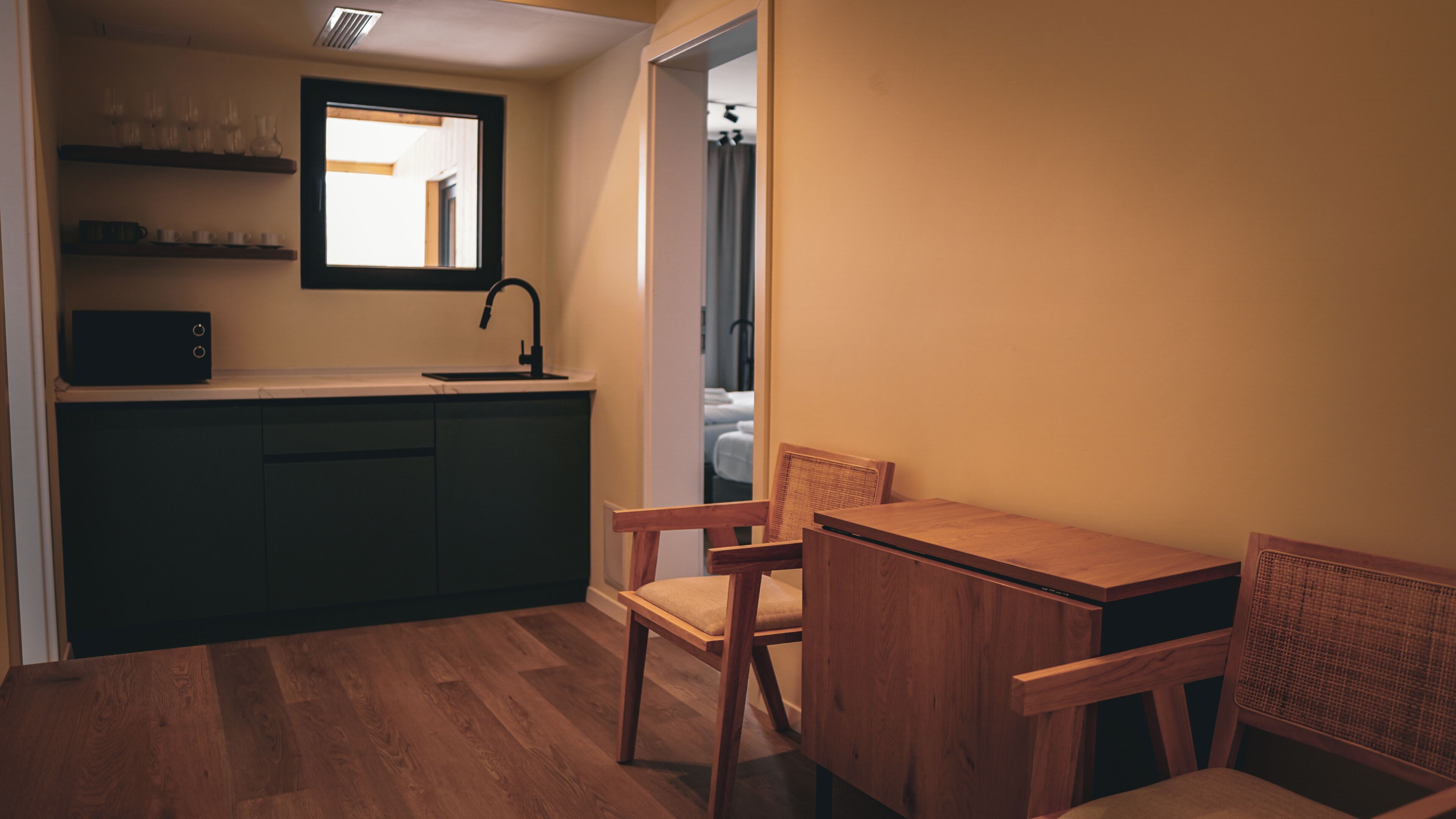 Una cocina compacta con armarios oscuros, una mesa de comedor de madera y una ventana con vista a un pasillo.