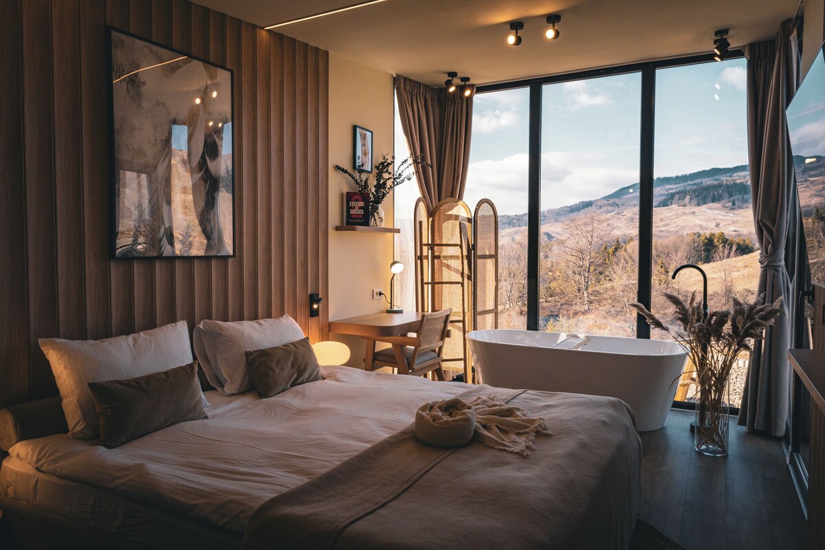 Un dormitorio moderno con una cama grande, una zona de estar con escritorio y una bañera.