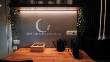 Un espacio de trabajo ordenado con una mesa de madera, una cafetera negra, una caja de madera y una pared con un diseño de luna creciente y una cita motivacional.