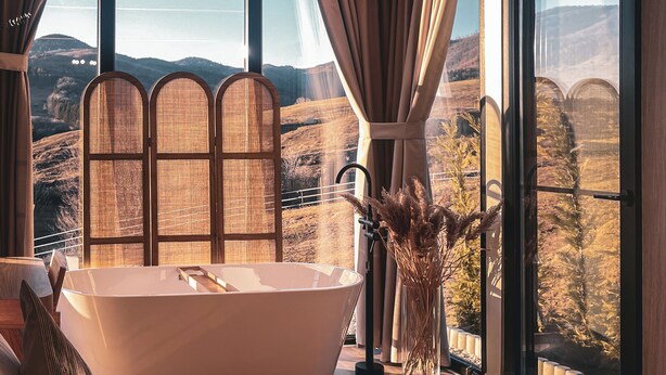 Una camera da letto con una grande finestra, una vasca da bagno e vista su un paesaggio montuoso.