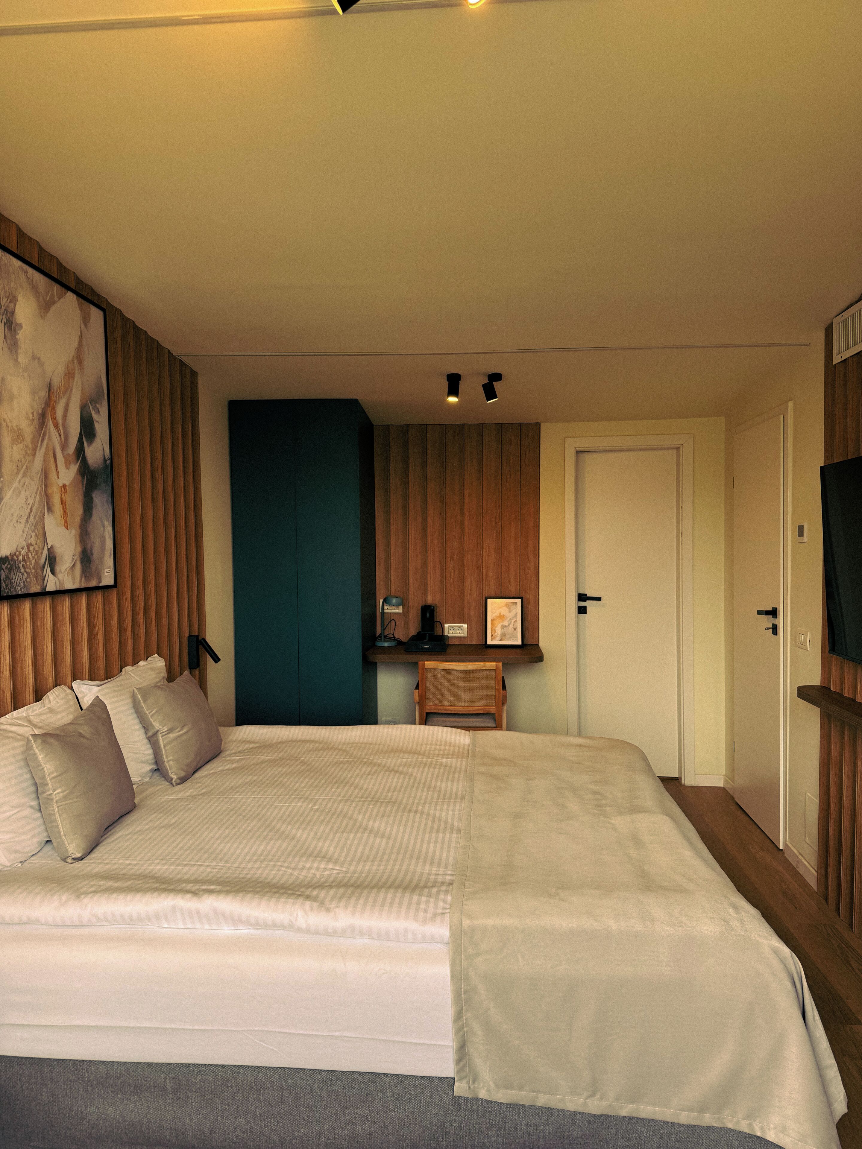 Ein Schlafzimmer mit einem großen Bett, einem Schreibtisch mit Stuhl, einem Fernseher und einer Tür.