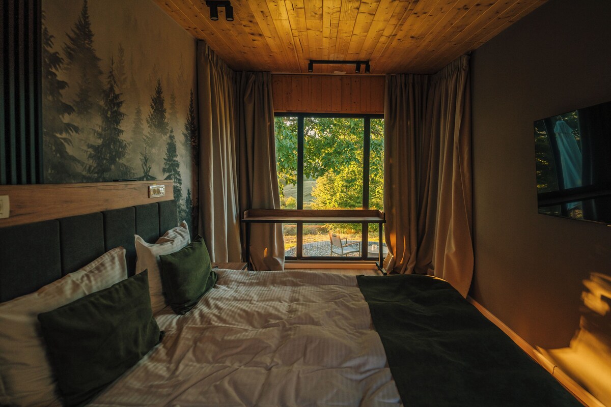 Ein Schlafzimmer mit einem großen Fenster, einem Bett mit Kissen, einem Kopfteil und einem Baumgemälde.